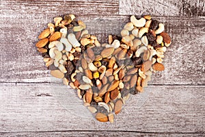 Mix of healthy raw nuts in heart shape on wooden background