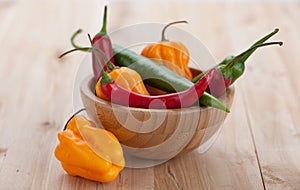 Mix of hottest peppers in wooden plate on table.