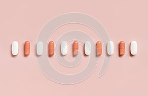 Mix of medical capsules in a line on light pink top view. Dietary supplements