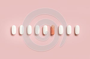 Mix of medical pills with one pink capsule in a line on light pink top view. Dietary supplements