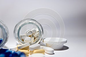 Mix of medicine pills and tablets scattered around glass bottle with some pills inside. Isolated on white background