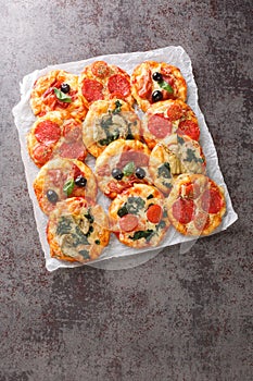 Mix mini pizza or Pizzette with various toppings close-up on parchment. Vertical top view photo