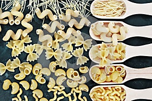 Mix of pasta shapes varieties on dark background: farfalle, macaroni, rigatoni, rotini, rigate