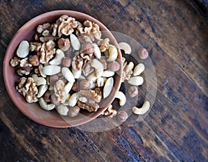 A mix of peeled dried fruit, with cashews, hazelnuts and walnuts, in a terracotta bowl on a weathered wooden table