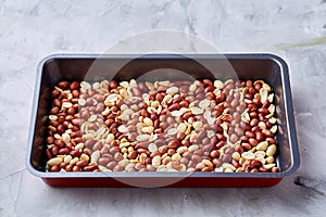 Mix of peeled raw peanut on baking tray over white textured background, selective focus, shallow depth of field.