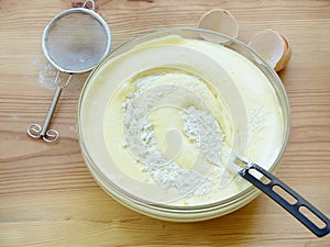 Mix pounded chicken egg yolks with the sugar, beaten egg whites and wheat flour in a glass bowl on a wooden background.