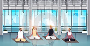 Mix race people sitting lotus position doing sport fitness exercises meditation relaxation concept modern gym interior