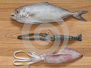 Mix seafood, black-banded trevally fish, tiger prawn, and cuttlefish, on wooden cutting board background