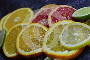 Mix of sliced colorful citrus fruits top view. Orange, lemon, grapefruit and lime half slices on black table.