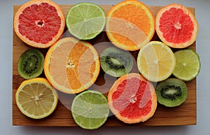 Mix of sliced colorful citrus fruits top view. Orange, lemon, kiwi, grapefruit and lime half slices on wooden board.