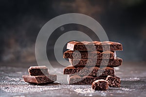 Mix stack of bitter and milky porous airy chocolate with cloud of cocoa on dark old background.