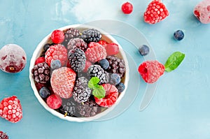 Mix of summer frozen berries in a white bowl on a blue concrete background. Copy space