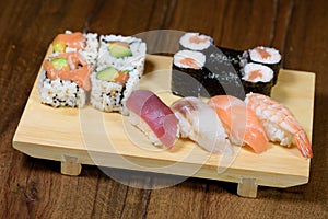 Mix of sushi, sushi roll and nigiri with salmon, tuna, sea bass, shrimp, avocado served on a wooden plate