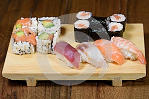 Mix of sushi, sushi roll and nigiri with salmon, tuna, sea bass, shrimp, avocado served on a wooden plate
