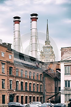 Mix of two pipes and buildings of different times against blue sky. Old Industrial building of the factory from red