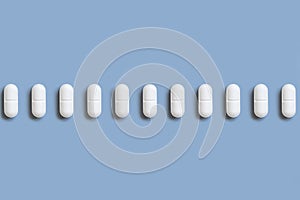 Mix of white medical pills in a line on light blue top view. Dietary supplements