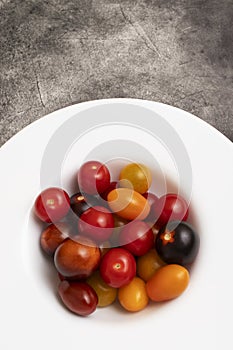 Mix of yellow, red and black cherry tomatoes in a white plate.