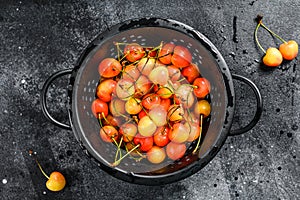 Mix of yellow and red ripe cherries in a colander. Black background. Top view