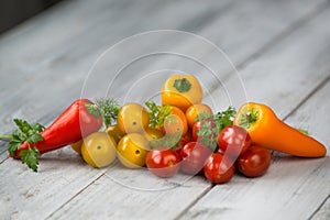 Mixed colored cherry tomatoes and mini paprika with fresh herbs on a wooden background