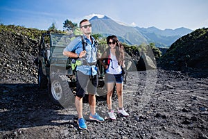 Mixed couple with knapshack in front of a jeep, outdoor activity