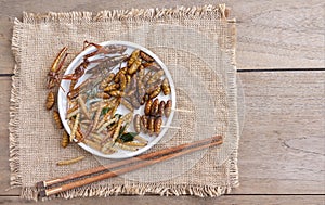 Mixed of crispy worm and insects in a ceramic plate with chopsticks on a wood table. The concept of protein food sources from