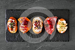Mixed crostini appetizers with a variety of toppings, top view on a dark slate background