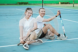 Mixed doubles tennis player sitting relaxed with racket