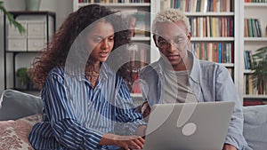 Mixed ethnic couple sit relax on couch in living room choose new goods on laptop