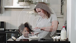 Mixed family baking - mom pours milk into a glass bowl for the dough making