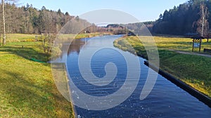 A mixed forest grows on the grassy banks of the river. The river makes a bend. Ripples appear on the water. In the autumn, leaves photo