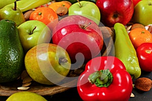 Mixed fruit - apples, pears, tangerines; and vegetable - peppers, tomatoes, avocados; with some whole almonds and nuts, closeup