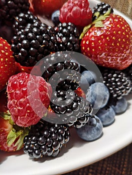 Mixed fruit berries on white plate. Closeup of forest fruits. Summer fruit