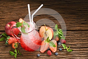 Mixed fruit juice with syrup and soda in glass pitcher surrounded by fruits on wooden table