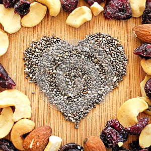 Mixed fruits,nuts, and chia seed heart on wood grain cutting board, arranged in square for social media, banners, and backgrounds.