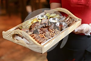 Mixed grilled meat with pepper sauce on a wooden board served by waiter in restaurant or diner