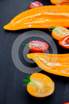 Mixed of half red and yellow pepper with a green branch near cherry tomato on black backround. Close up.