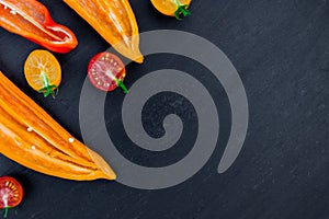 Mixed of half red and yellow pepper with a green branch near cherry tomato on black backround. Top view. Frame. Copy space.