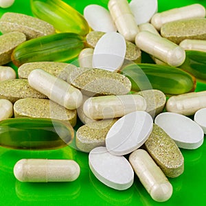 Mixed natural food supplement pills, omega 3, calcium, multivitamin and glucosamine capsules on green background.