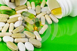 Mixed natural food supplement pills, omega 3, calcium, multivitamin and glucosamine capsules on green background.