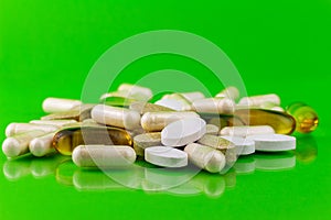 Mixed natural food supplement pills, omega 3, calcium, multivitamin and glucosamine capsules on green background.