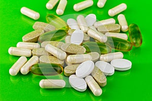 Mixed natural food supplement pills, omega 3, calcium, multivitamin and glucosamine capsules on green background.