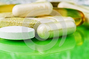 Mixed natural food supplement pills, omega 3, calcium, multivitamin and glucosamine capsules on green background.