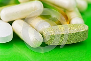 Mixed natural food supplement pills, omega 3, calcium, multivitamin and glucosamine capsules on green background.