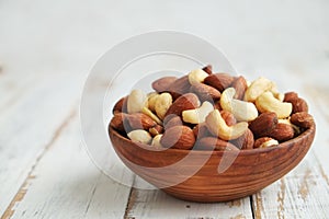 Mixed nuts in a bowl on a white wooden background.