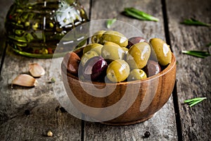 Mixed olives in a bowl with rosemary, olive oil and garlic on a rustic table