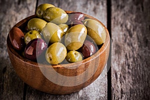 Mixed olives in a wooden bowl closeup on a rustic table