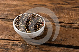 Mixed peppercorns in bowl on vintage wooden background.