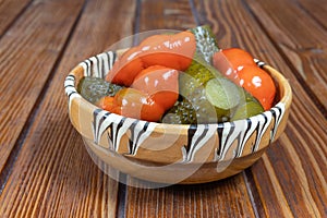 Mixed pickles of cucumbers and red bell peppers. Pickles in Romanian traditional clay bowl on wooden table.