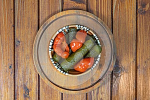 Mixed pickles of cucumbers and red bell peppers. Pickles in Romanian traditional clay bowl on wooden table.