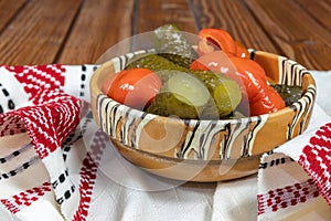 Mixed pickles of cucumbers and red bell peppers. Pickles in Romanian traditional clay bowl on wooden table.